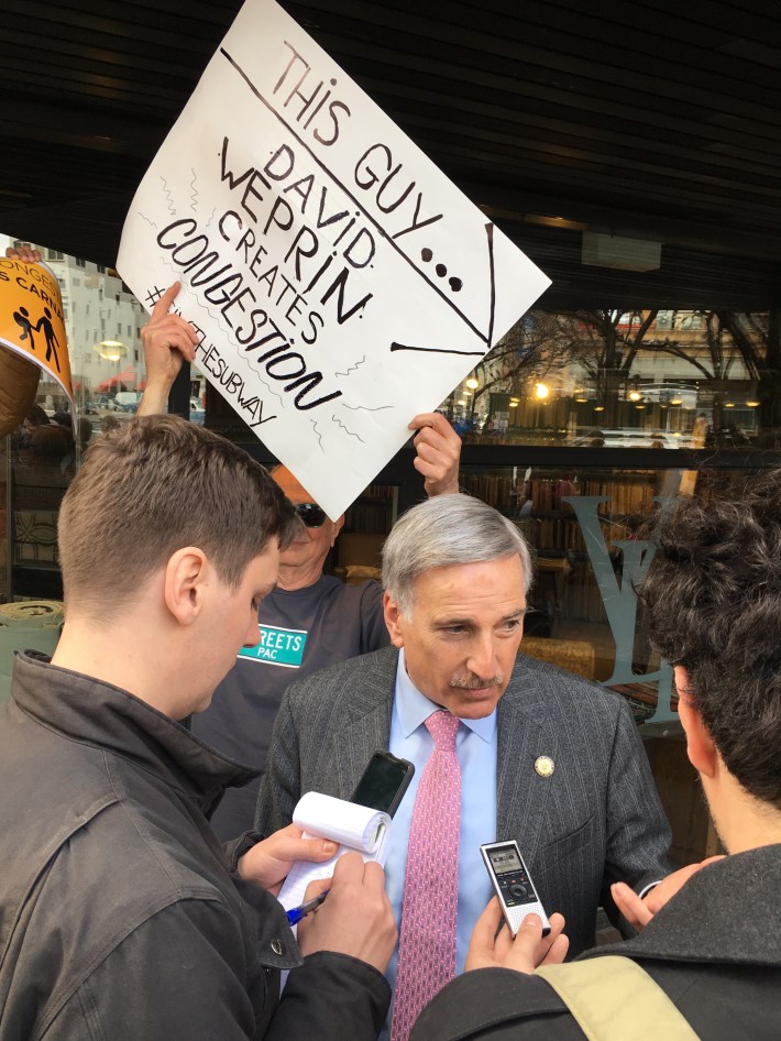 David Weprin talks to reporters Clayton Guse and Vin Barone as a protester makes his point.